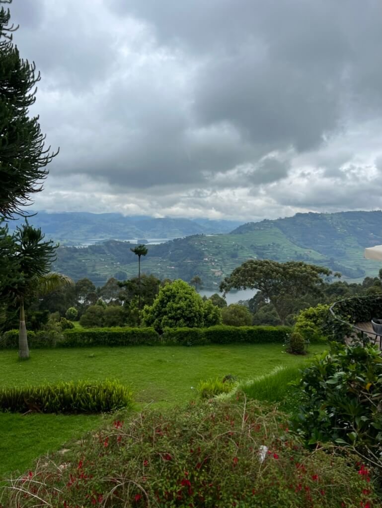 A lush green landscape with a variety of trees and shrubs overlooks distant hills under a cloudy sky. The scene conveys a tranquil and verdant countryside. Uganda Amatsiko Tours