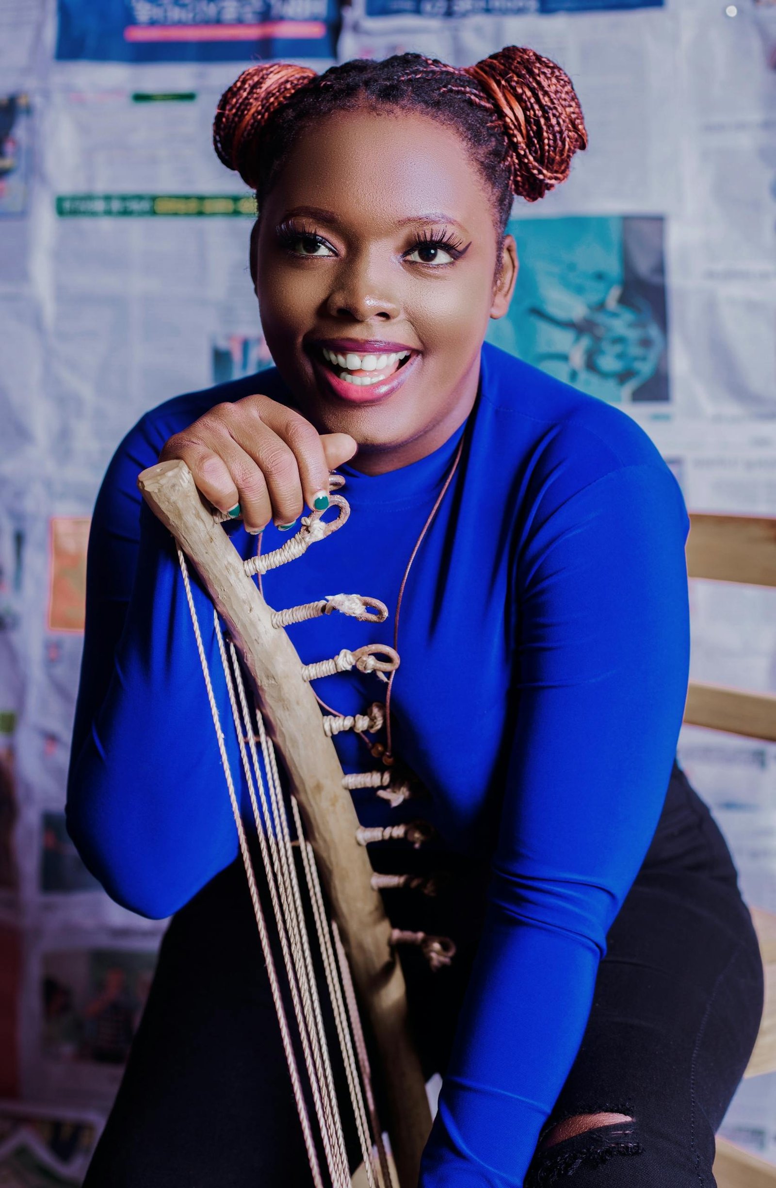 A joyful woman smiles while holding a traditional African musical instrument indoors.