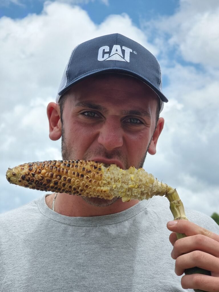 Back-to-Basics Nature Experience- A guest eating a roasted maize with a cap on his head