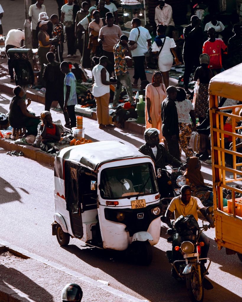 Bustling street market in Kampala, Uganda, showcasing local vendors, pedestrians, and a tuk tuk on a sunny day.