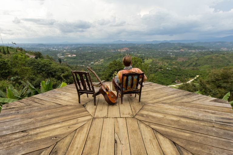 A person enjoys a scenic mountain- view while seated on a wooden deck with a guitar. Uganda Travel